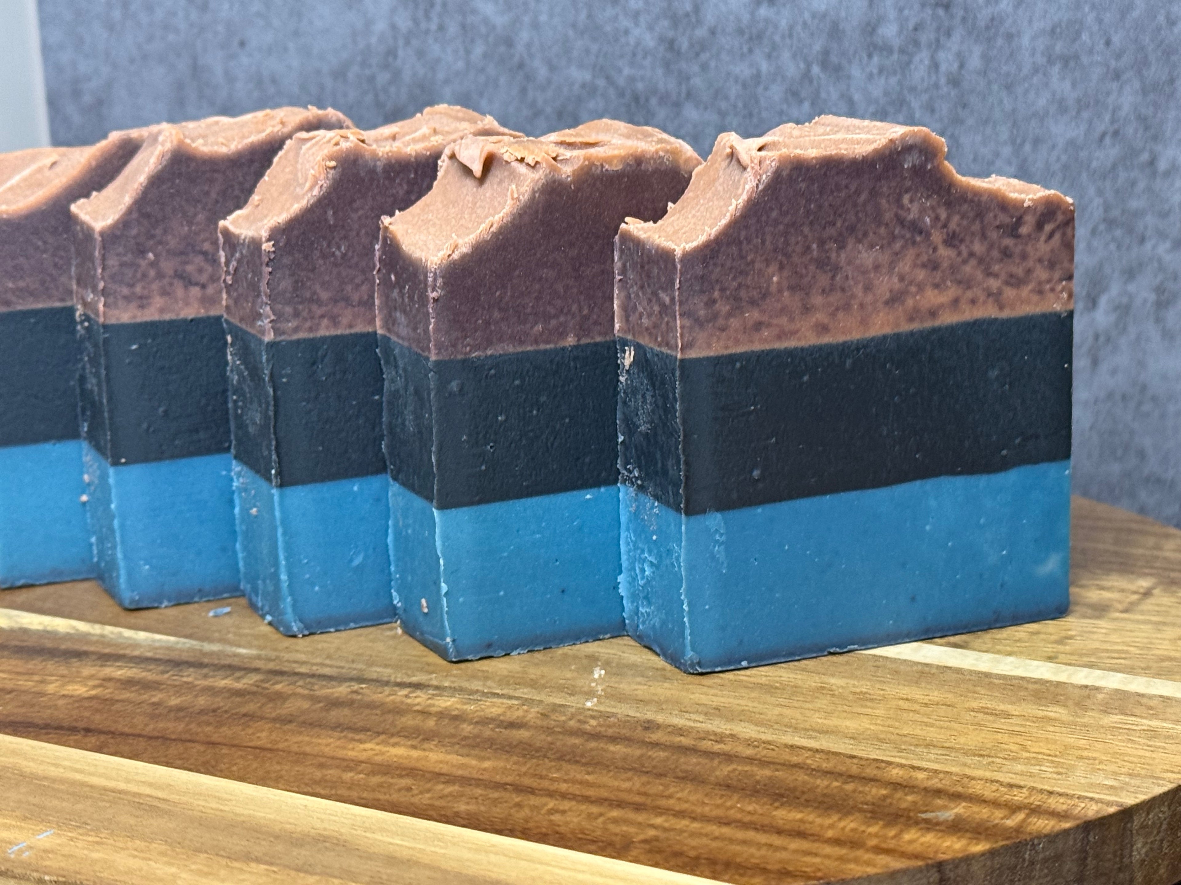 Four layered soap bars with brown, black, and blue sections on a wooden surface.